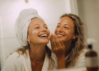 Dos jóvenes europeas aplicándose crema hidratante para el frío durante su rutina matutina de invierno con luz natural de ventana