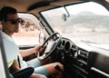 A professional van driver reviewing tachograph rules compliance data on a smart device inside a light commercial vehicle cab