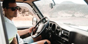 A professional van driver reviewing tachograph rules compliance data on a smart device inside a light commercial vehicle cab