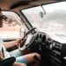 A professional van driver reviewing tachograph rules compliance data on a smart device inside a light commercial vehicle cab