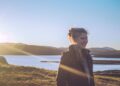 A woman stands in soft June daylight during a Nordic summer morning, her face turned toward the light in a moment of calm wellbeing.