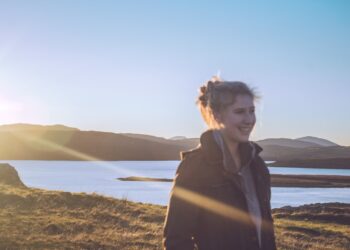Eine Frau steht im weichen Juni-Tageslicht während eines nordischen Sommermorgens, ihr Gesicht dem Licht zugewandt in einem Moment ruhigen Wohlbefindens.