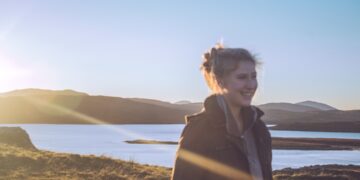 A woman stands in soft June daylight during a Nordic summer morning, her face turned toward the light in a moment of calm wellbeing.