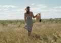 A woman wearing a flowing natural linen dress from one of Europe's leading linen brands, standing in warm summer light