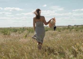 A woman wearing a flowing natural linen dress from one of Europe's leading linen brands, standing in warm summer light