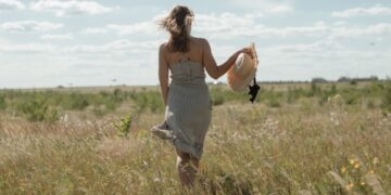 A woman wearing a flowing natural linen dress from one of Europe's leading linen brands, standing in warm summer light