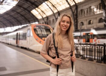 A young woman boarding a train in Europe holding her phone with rail passes ready to show