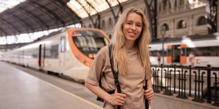 A young woman boarding a train in Europe holding her phone with rail passes ready to show