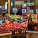 A woman selecting fresh seasonal vegetables at an EU summer farmers market in a sunlit town square.