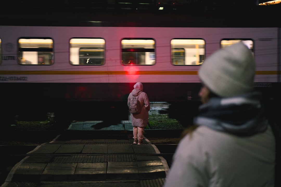 A couple boarding overnight trains at a European station platform, luggage in hand, city lights behind them