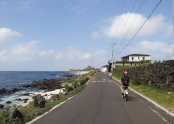 A cyclist on a certified EU coastal cycling route rides along a cliff-top path with the sea visible below