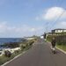 A cyclist on a certified EU coastal cycling route rides along a cliff-top path with the sea visible below