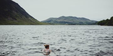 A swimmer wading into a certified EU open-water lake on a clear summer morning, with safety buoys visible in the background.