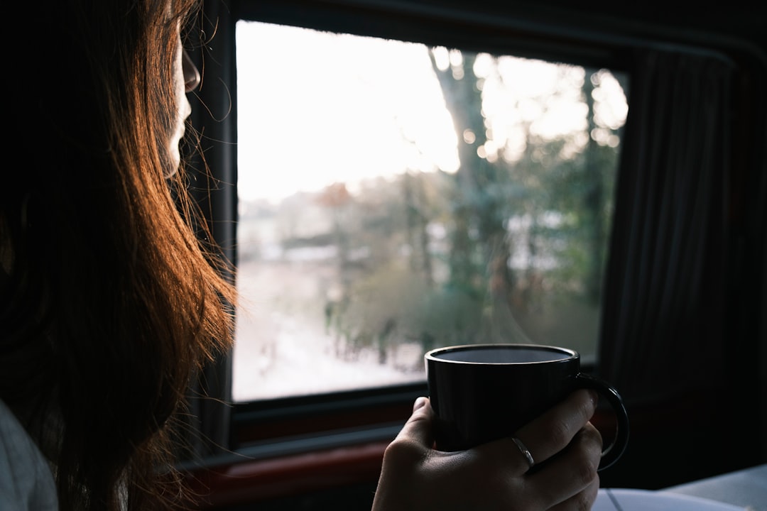 A traveler with a coffee cup looking out the window of overnight trains as they arrive in a new European city at dawn
