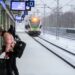 A woman boarding a European train, choosing rail travel to reduce her carbon footprint on a summer holiday