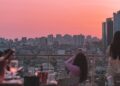 A woman enjoying dinner at one of the most elegant rooftop restaurants in Paris, with the city skyline glowing at sunset