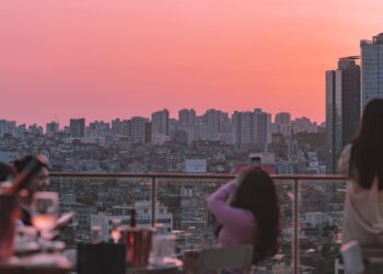 A woman enjoying dinner at one of the most elegant rooftop restaurants in Paris, with the city skyline glowing at sunset
