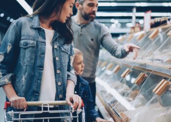 A woman carefully reading the label on certified gluten-free pasta in a European supermarket aisle