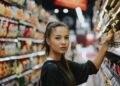 A woman carefully reading the packaging of an EU Ecolabel certified household cleaning product in a supermarket aisle.