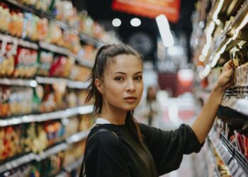 A woman carefully reading the packaging of an EU Ecolabel certified household cleaning product in a supermarket aisle.