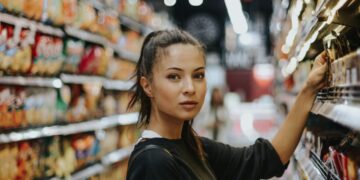 A woman carefully reading the packaging of an EU Ecolabel certified household cleaning product in a supermarket aisle.