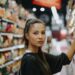 A woman carefully reading the packaging of an EU Ecolabel certified household cleaning product in a supermarket aisle.
