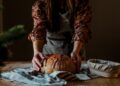 A baker proudly presents a rustic wheat-free bread loaf in a traditional European artisan bakery