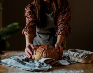 A baker proudly presents a rustic wheat-free bread loaf in a traditional European artisan bakery