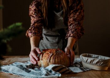 A baker proudly presents a rustic wheat-free bread loaf in a traditional European artisan bakery
