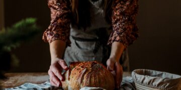 A baker proudly presents a rustic wheat-free bread loaf in a traditional European artisan bakery