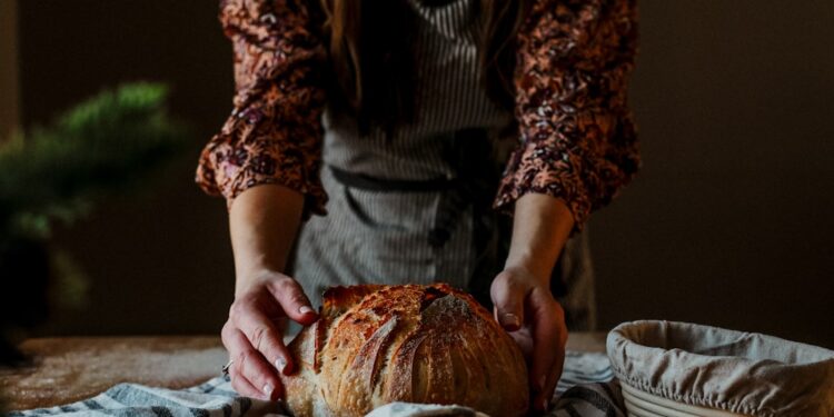 baker-woman-holding-buckwheat-loaf-unsplash - EUwebzine A baker proudly presents a rustic wheat-free bread loaf in a traditional European artisan bakery