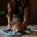 A baker proudly presents a rustic wheat-free bread loaf in a traditional European artisan bakery
