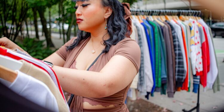 A woman reviews garments at an EU circular fashion sample sale, looking for certified-organic pieces at reduced prices.
