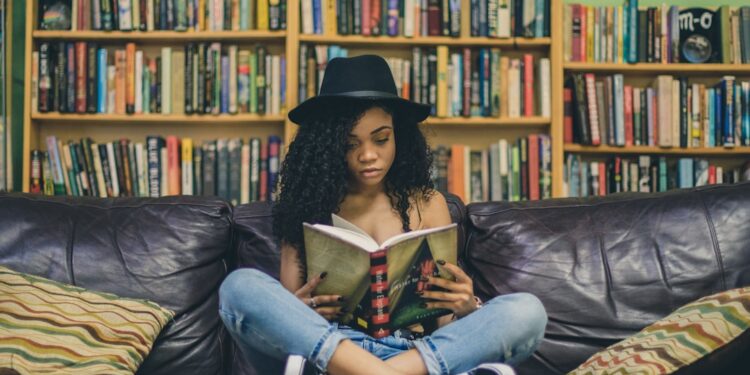 A woman reads a minority language poetry collection in a European library, surrounded by shelves of multilingual literary.