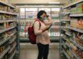A woman carefully reading the EU Ecolabel flower logo on a cleaning product in a European supermarket aisle