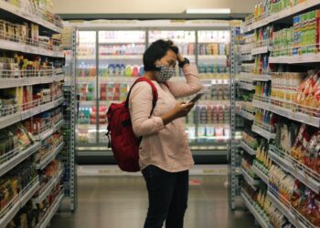 A woman carefully reading the EU Ecolabel flower logo on a cleaning product in a European supermarket aisle