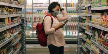 A woman carefully reading the EU Ecolabel flower logo on a cleaning product in a European supermarket aisle