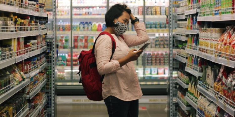 A woman carefully reading the EU Ecolabel flower logo on a cleaning product in a European supermarket aisle