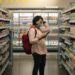 A woman carefully reading the EU Ecolabel flower logo on a cleaning product in a European supermarket aisle