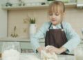 A young child learning bread-making techniques during harvest workshops at a traditional European rural farm