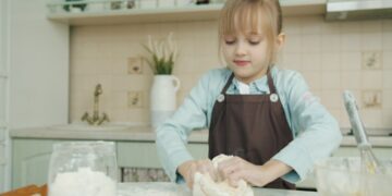 A young child learning bread-making techniques during harvest workshops at a traditional European rural farm