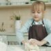 A young child learning bread-making techniques during harvest workshops at a traditional European rural farm