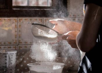 A woman home baker reading the label on a bag of EU-certified gluten-free flours in a bright autumn kitchen