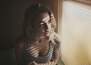 A woman standing by a bright window in autumn morning light, actively resetting her daily rhythm with natural light exposure.