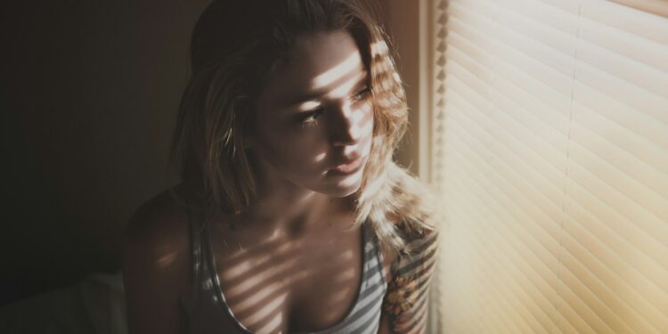 A woman standing by a bright window in autumn morning light, actively resetting her daily rhythm with natural light exposure.
