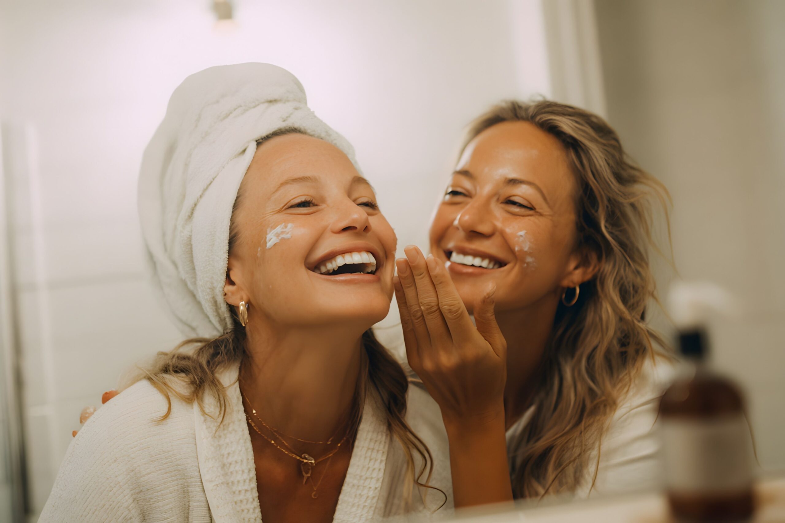 Duas jovens europeias aplicando hidratante de cuidados com a pele para clima frio durante a rotina matinal de inverno com iluminação natural de janela