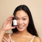 A woman carefully applying a serum containing EU skincare ingredients in a minimalist bathroom setting