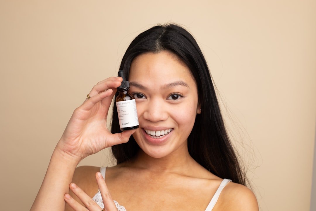 Uma mulher a aplicar cuidadosamente um sérum contendo ingredientes de cuidados de pele da UE num ambiente de casa de banho minimalista