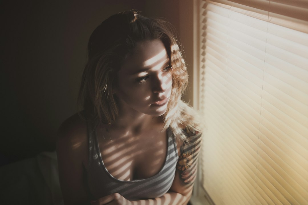 Uma mulher de pé junto a uma janela brilhante à luz da manhã de outono, a repor ativamente o seu ritmo diário com exposição à luz natural.